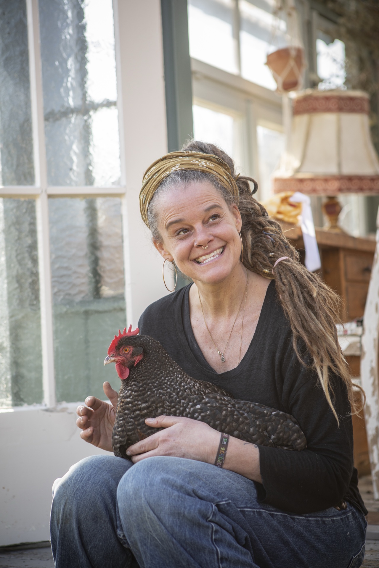 Nico Simmeth mit lachendem Gesicht hält ein schwarzes Huhn auf dem Schoß in der Orangerie